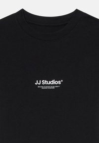 Čierne bavlnené tričko s okrúhlym výstrihom. Na prednej strane je biely text, ktorý obsahuje "JJ Studios" a ďalšie podrobnosti o značke pod ním.