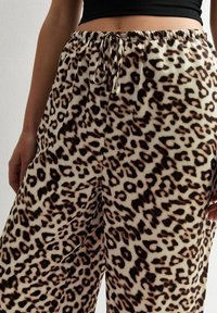 Leopardenmuster, weite Hose. Leichter Stoff mit einem elastischen Bund, der eine Kordel hat. Farben sind Beige, Braun und Schwarz.