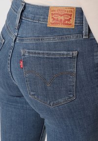Jeans de mezclilla azul con cintura alta, parche trasero con "Levi Strauss & Co" y costuras curvas distintivas en los bolsillos traseros.