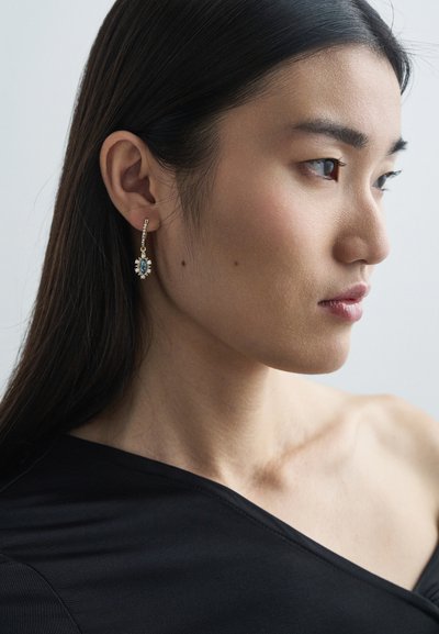 Gold-tone drop earrings featuring a central turquoise stone surrounded by smaller clear stones, adding a delicate sparkle.
