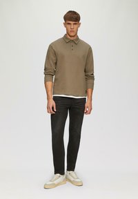 Polo-shirt à manches longues vert olive avec un col, associé à un jean slim noir et des baskets de couleur claire. Design simple, sans motifs.