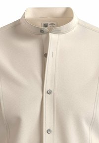 Camicia beige strutturata con colletto alzato, caratterizzata da cinque bottoni sul davanti e dettagli di cuciture sottili. Il tessuto ha una finitura liscia.