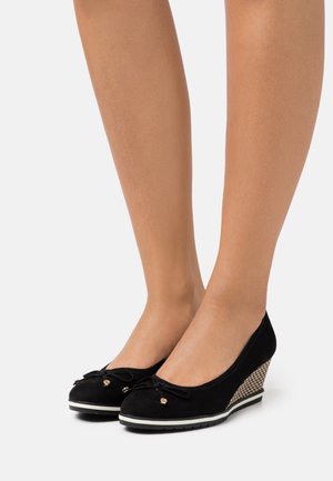 Zapatos de cuña de ante negro con punta redonda, lazo decorativo y acentos dorados; tacón de cuña de tejido texturizado y suela de goma blanca.