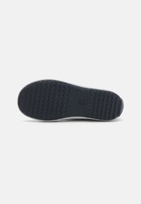 Semelle en caoutchouc de sneaker navy avec un motif zigzag texturé, dotée d'un talon plat et arrondi et d'un logo central en relief sur un matériau foncé.