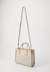 Bolsa retangular bege com alças curtas e uma alça de ombro longa e ajustável, apresentada contra um fundo branco liso.