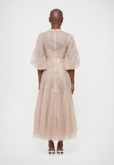 Sukienka midi o luźnym kroju w jasnobeżowym tiulu, zdobiona kropkowanym wzorem, z dzwonkowymi rękawami i ukrytym zamkiem błyskawicznym z tyłu. Obcasy widoczne poniżej brzegów.