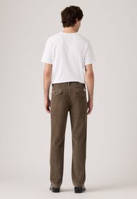 Pantaloni in velluto a coste marroni con vestibilità dritta, due tasche posteriori e dettagli del logo discreti. Abbinati con una t-shirt bianca semplice.