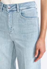 Jeans de denim azul claro con un diseño de pierna recta, que cuentan con bolsillos delanteros y un cierre de botón visible en la cintura. Textura suave.