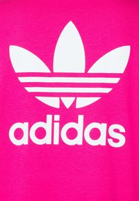 Fuksjowa koszulka z dużym białym logo Adidas, z trzema paskami i wzorem trefoila. Gładka faktura i luźny krój.