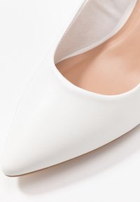 Scarpa piatta bianca a punta, realizzata in materiale sintetico testurizzato. Presenta una fodera interna liscia e una suola bassa di colore marrone chiaro.