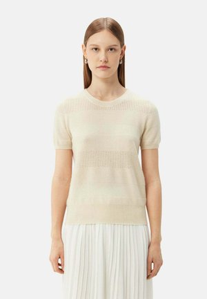Hellbeige, gestrickter Pullover mit kurzen Ärmeln, der horizontale Strukturmuster und einen runden Ausschnitt aufweist, getragen über einem plissierten weißen Rock.