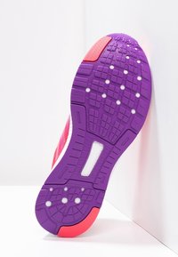 Semelle de chaussure de sport en violet avec des accents roses, présentant un motif de grip texturé et des trous ronds pour la respirabilité. Formes triangulaires et rectangulaires.