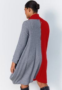 Robe tricotée avec un design asymétrique, présentant un tissu texturé gris d'un côté et un rouge uni de l'autre, accentuée par une fermeture éclair à l'arrière.