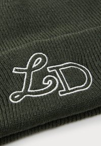 Grønn strikket lue med hvit brodert "LD" logo. Stoffet har en ribbet tekstur og tettsittende passform, egnet for kaldt vær.