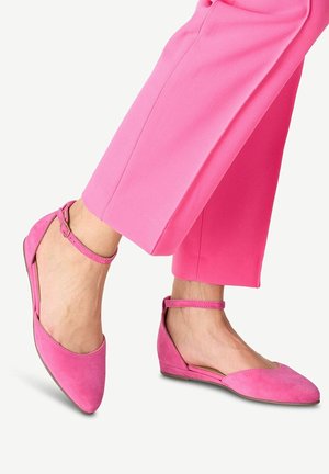 Fødder iført lyserøde flats med ankelrem, kombineret med matchende lyserøde cropped bukser mod en ensfarvet baggrund.