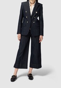 Tmavě modrý denimový blazer s dvojitým zapínáním, zlatými knoflíky, kombinovaný s volnými tmavě modrými denimovými kalhotami, doplněný kontrastním prošitím.