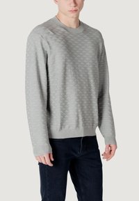 Grijze sweatshirt met diamantpatroon textuur, geribbelde ronde hals en manchetten, gecombineerd met donkere jeans, getoond op een effen achtergrond.