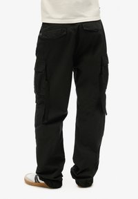 Zwarte cargobroek met meerdere zijzakken, een losse pasvorm en een gladde stoftextuur. Achteraanzicht benadrukt de zakdetails.