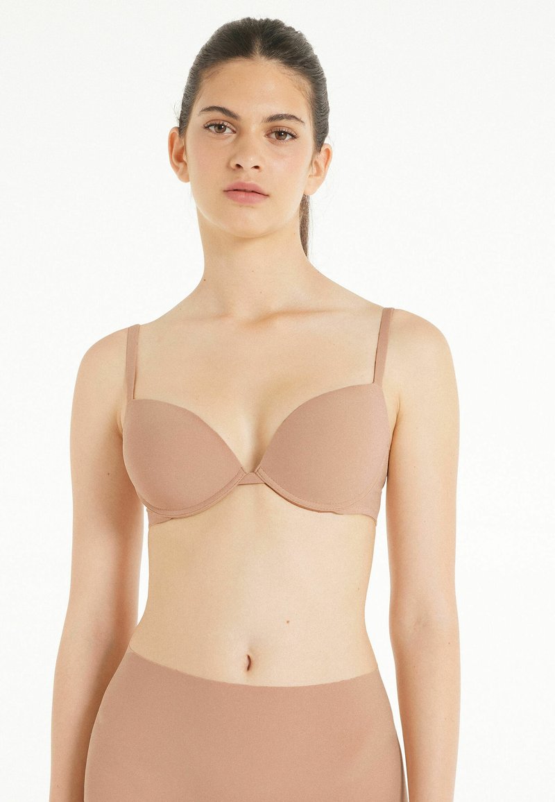 Světle hnědá vycpaná podprsenka s nastavovacími ramínky, hladkým povrchem a bezešvým designem. Vhodná pro minimalistický vzhled spodního prádla.