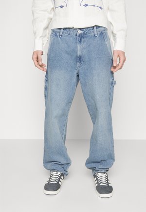 Light blue denim cargo pants with a relaxed fit, featuring side pockets and a waistband with belt loops. Paired with gray and white sneakers.