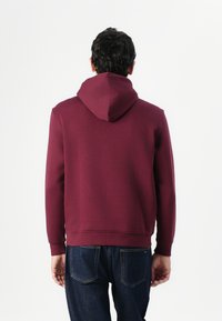 Bordeaux hættebluse med en glat tekstur, tætsiddende manchetter og ribbet kant, parret med mørkeblå denim jeans.