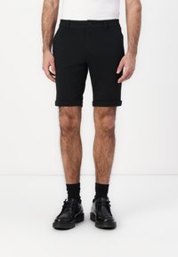 Pantaloni corti neri sartoriali realizzati in un tessuto liscio, con chiusura a bottone, risvolti arrotolati e un design slim fit, abbinati a scarpe eleganti nere.