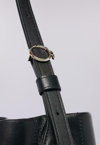 Svart läderband med en glänsande guldring i metall, med en strukturerad yta och en slät ände med spänndetalj.