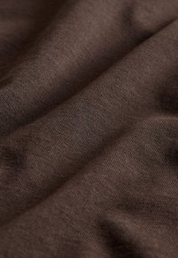 Close-up af blødt, brunt, ribbet stof med synlig tekstur og blide folder, der skaber et bølget mønster.