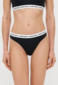 Zwarte katoenen string met een witte elastische tailleband waarop "BJÖRN BORG" branding staat. Gladde textuur, aansluitend ontwerp, minimale bedekking.