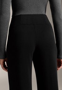 Crne hlače s visokim strukom, glatke teksture i uskog kroja, uparene sa sivom rebrastom majicom dugih rukava.