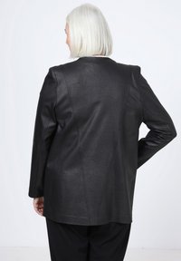 Veste en cuir noir avec une finition texturée, présentant une coupe ajustée, des manches longues et des lignes épurées, vue de dos.