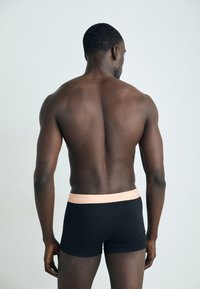 Crne bokserice s kontrastnim svijetloružičastim pojasom na kojem se ističe natpis "Calvin Klein", s glatkim, prilagođenim dizajnom.