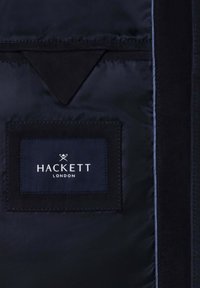 Tmavě modrý podšívka bundy s přišitou štítkovou látkou Hackett London a trojúhelníkovým látkovým detailem nad štítkem.