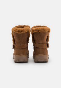Bottines en daim marron avec une doublure en fausse fourrure et un col repliable, dotées d'une sangle et d'une boucle, ainsi que de semelles en caoutchouc texturé.