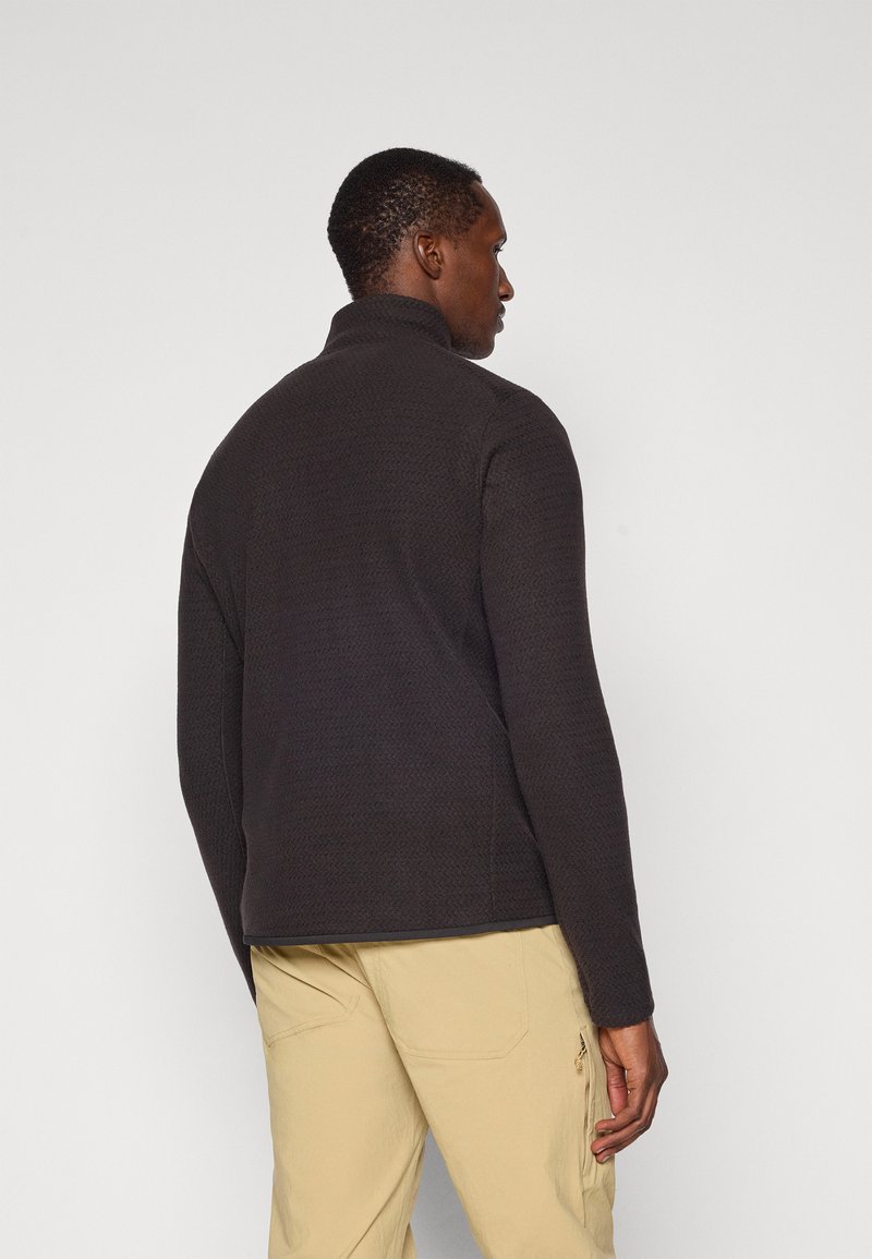 Schwarze Fleece-Jacke mit hohem Kragen und strukturiertem Stoff. Das Design verfügt über eine figurbetonte Silhouette und lange Ärmel.