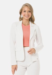 Weißer gerippter Blazer mit einer einzelnen Tasche, kombiniert mit einem rosa gerippten Cropped-Top. Der Blazer verfügt über einen geschlitzten Kragen und eine schmale Passform.