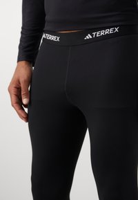 Sorte svarte treningsleggings med elastisk stoff, utstyrt med en TERREX-merket midjebånd. Glatt tekstur og tettsittende design for komfort.