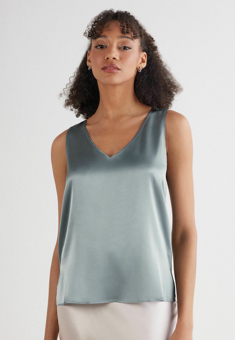 Halenka bez rukávů ve tvaru V z jemné, tlumené zelené saténové látky s hladkým povrchem a čistými okraji, která má volný střih.