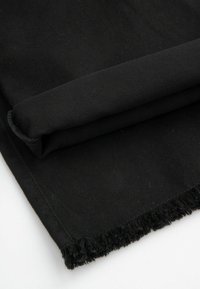 Czarna bawełniana tkanina o gładkiej fakturze, z postrzępionymi brzegami. Zrolowana na jednym końcu dla swobodnego wyglądu.