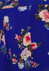 Tissu bleu avec un motif floral comprenant des fleurs roses, blanches et brunes. La texture est lisse avec des détails de couture visibles.