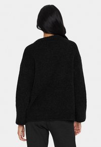 Crni, teksturirani džemper s dugim rukavima i opuštenim krojem. Ima okrugli izrez i mekan, perast materijal.