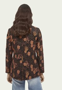Czarna kurtka z długimi rękawami, ozdobiona skomplikowanymi wzorami florystycznymi i zwierzęcymi w odcieniach pomarańczowego i złotego. Gładka, teksturowana tkanina o dopasowanym kroju.