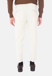 Pantaloni bianchi a sigaretta con girovita piatto e tasche posteriori, caratterizzati da orli a risvolto. Abbinati a scarpe marroni e un maglione marrone.