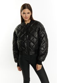 Sort quiltet pufferjakke med lynlås foran, ribbede manchetter og cropped design. Fremstillet af skinnende, let materiale.