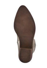 Suela de goma marrón con un patrón de textura, con forma redondeada. Parte superior del zapato en beige claro con sutil textura y detalle de costura.