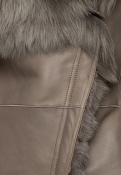 Materiale in pelle marrone con un morbido bordo in pelliccia. Presenta cuciture a vista e una superficie texturizzata, evidenziando la combinazione di texture.