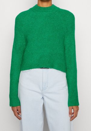 Zielony sweter z dzianiny o prążkowanej fakturze, okrągłym dekolcie i krótkim kroju. W zestawieniu z jasnoniebieskimi jeansami o wysokim stanie.