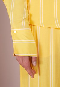 Camicia a maniche lunghe gialla a righe con strisce bianche, dotata di un dettaglio con polsino abbottonato e un tessuto morbido e texturizzato.