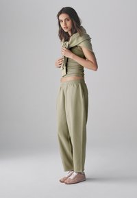 Top verde chiaro aderente con maniche corte, pantaloni della tuta larghi abbinati e scarpe da ginnastica rosa. Maglione drappeggiato sulle spalle, tessuto texturizzato.