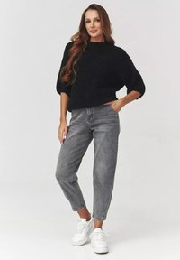 Czarny dzianinowy sweter o luźnym kroju, zestawiony z szarymi spodniami typu high-waist i białymi trampkami. Gładka faktura, casualowy design.